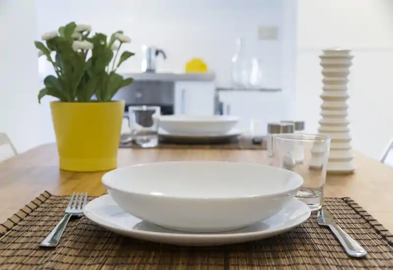 Mesa de comedor puesta con vajilla, superficie de madera, cristalería y una planta en maceta — zona de comedor luminosa y moderna.