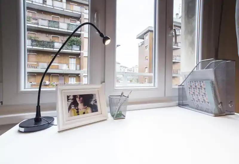 Coin bureau lumineux et épuré près de grandes fenêtres, avec lampe de lecture, photo encadrée et organiseur — idéal comme coin bureau ou coiffeuse dans une chambre.