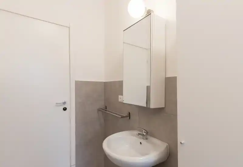 Compact bathroom with a wall-mounted sink, mirrored cabinet and towel rail; neutral tile wainscot and a bright wall light create a clean, functional feel.