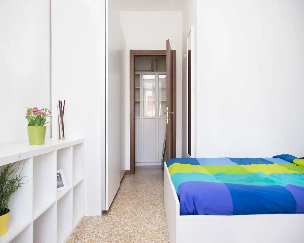 Camera da letto luminosa e moderna con letto colorato, armadiature incassate e piante decorative che creano un'atmosfera pulita e fresca.