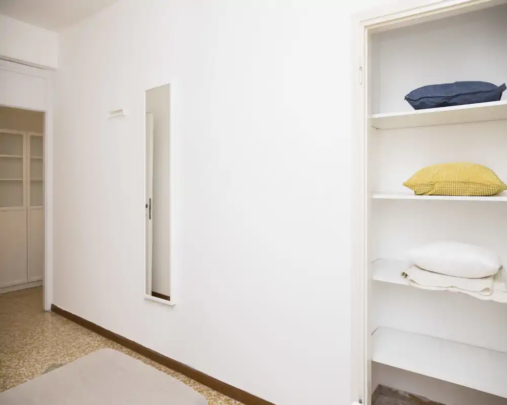 Ingresso o piccolo corridoio minimalista con pareti bianche, un sottile specchio a figura intera e scaffali aperti con cuscini e biancheria.