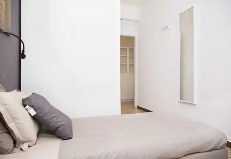 Camera da letto minimalista con letto matrimoniale rifatto, biancheria neutra e morbidi cuscini; pareti bianche e arredo essenziale creano un ambiente tranquillo e luminoso.