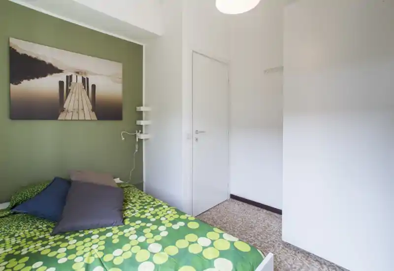 Chambre compacte avec mur vert, couette à motifs verts et coussins superposés ; une décoration murale et une lumière douce créent une atmosphère calme et chaleureuse.