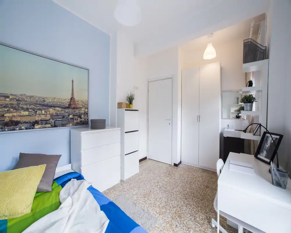 Bright, tidy bedroom with a visible single bed, desk area and wardrobe. The room features soft blue walls, organized storage and natural light, ideal for a single tenant.