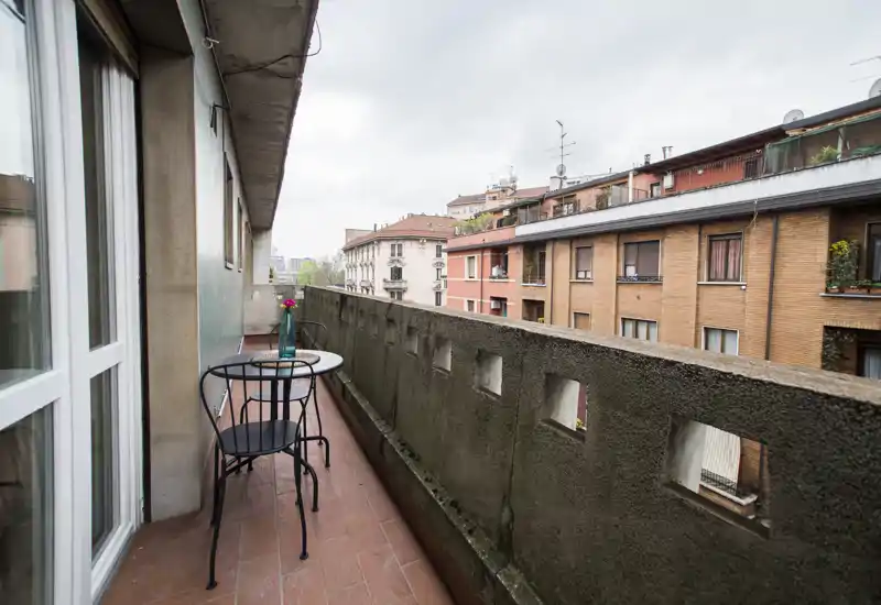 Sunny city balcony with a small table and two chairs, ideal for morning coffee and views over neighboring buildings.
