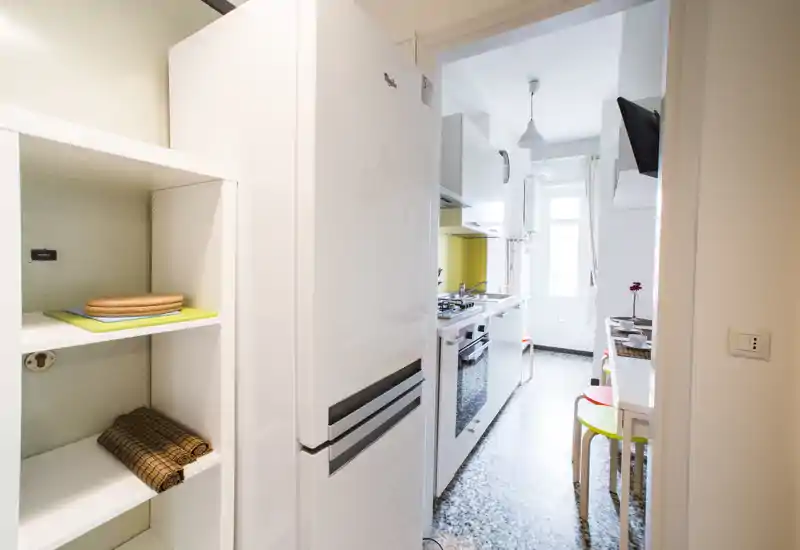 Bright, narrow modern kitchen with white cabinets, refrigerator, gas stove and a small breakfast area by the window.