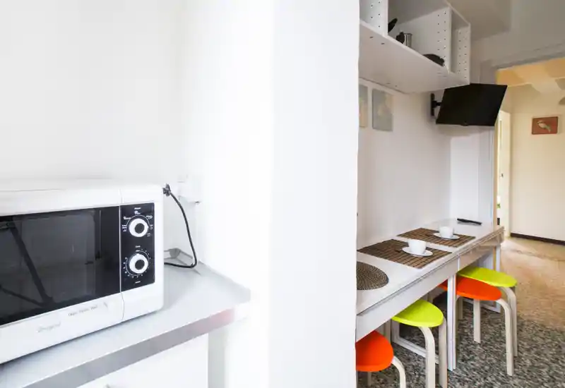 Compact, modern kitchenette with a white microwave, a narrow breakfast bar set with placemats and cups, and colorful stools — bright and neatly arranged for quick meals.