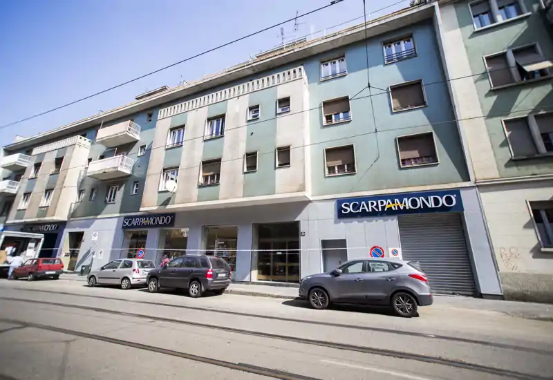 Street-facing building façade with ground-floor retail (SCARPAMONDO), parked cars and tram rails; clear daylight exterior shot suitable for a neighborhood listing.