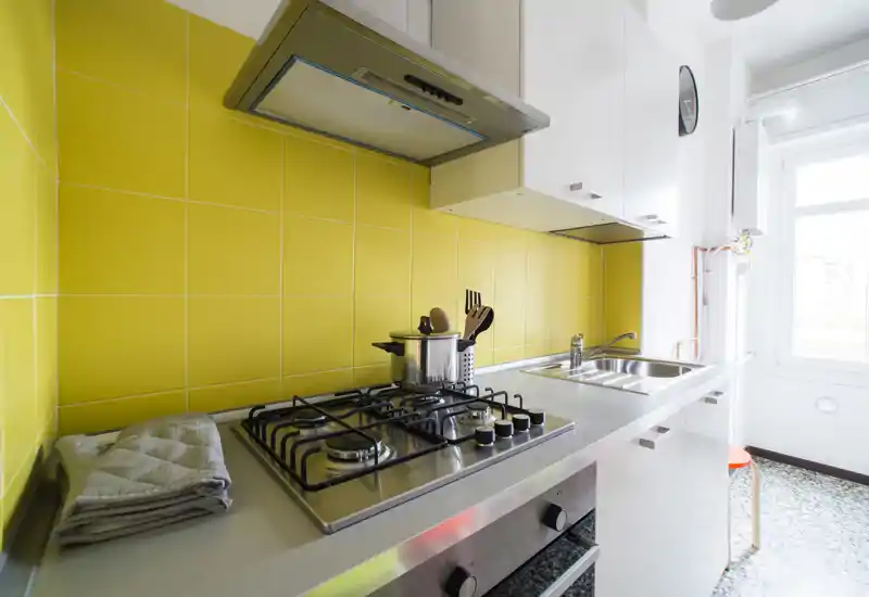 Bright modern kitchen with a stainless steel gas hob, sink, and a cheerful yellow tiled backsplash. Well-lit and neatly styled, ideal for compact apartment listings.