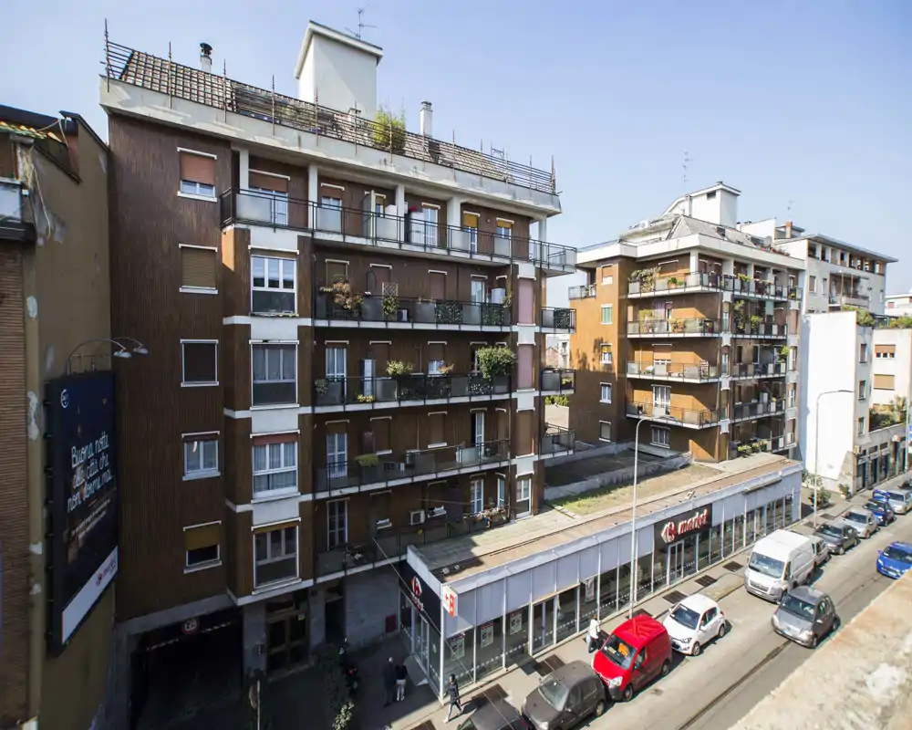 Vue extérieure au niveau de la rue d'immeubles résidentiels avec balcons et commerce en rez-de-chaussée ; lumière du jour claire, idéale pour montrer l'emplacement et l'animation de la rue.