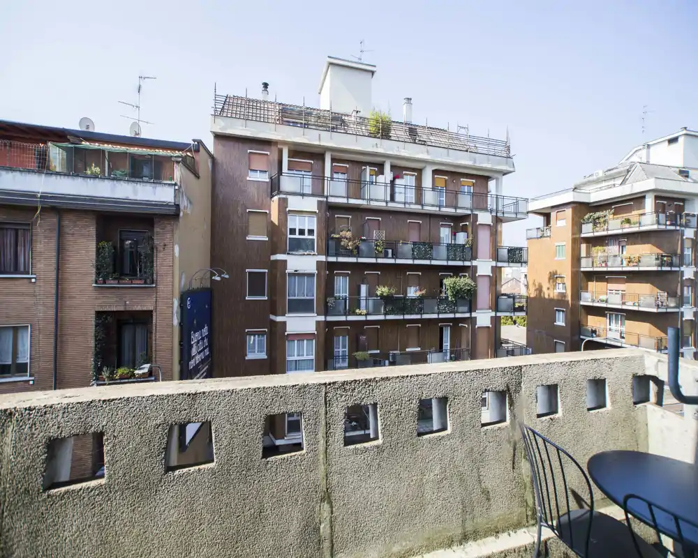 Balcon ensoleillé donnant sur les immeubles voisins ; petite table et chaises visibles au premier plan et belle lumière naturelle.