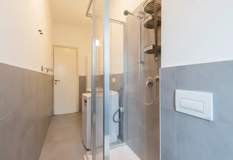 Compact modern bathroom with a glass-enclosed shower, tiled walls and a wall-mounted flush plate. The photo shows fixtures and finishes clearly, suitable for listing details.