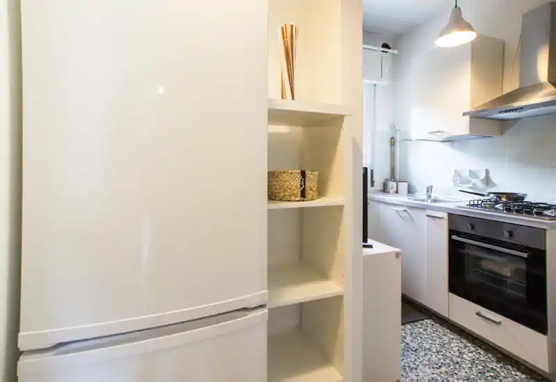 Bright modern kitchen with built-in oven, gas hob, sink and tidy open shelving — compact and efficiently arranged for everyday cooking.