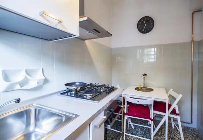 Compact modern kitchen with a stainless sink, gas hob and a small dining table with red-cushioned chairs — bright, clean and efficiently arranged for city living.