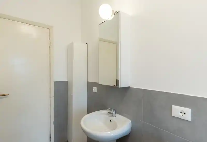 Compact modern bathroom corner with a wall-mounted sink, mirrored cabinet and neutral grey tiles — well lit and uncluttered.