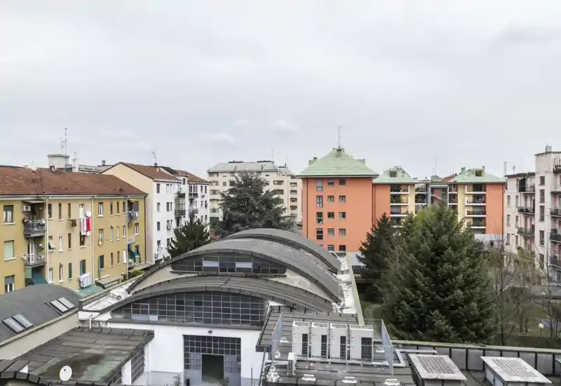 Exterior urban view showing rooftops and apartment blocks from a higher floor; overcast sky and greenery in the courtyard are visible.