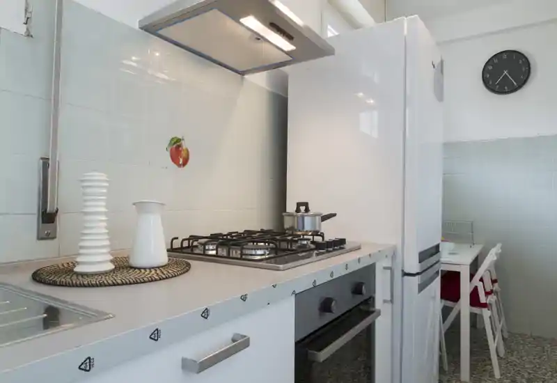 Bright, compact kitchen with a gas cooktop, oven and refrigerator. Clean tiled walls and a small dining nook make this space practical and inviting for everyday meals.