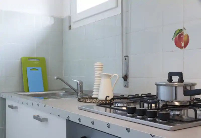 Bright, tidy kitchen counter with a stainless sink, gas stove and decorative pitcher — ideal for rental listings highlighting a functional kitchenette.
