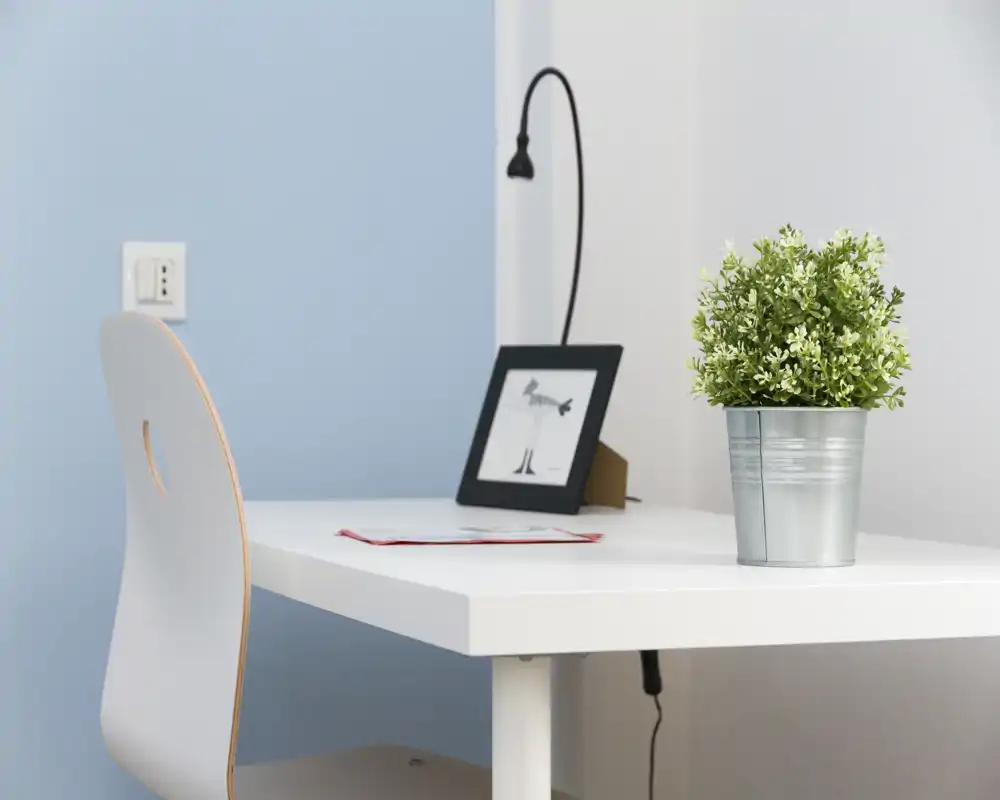 Area lavoro luminosa e minimale con scrivania bianca, sedia semplice, pianta in vaso e una lampada da scrivania — perfetta per studiare o lavorare.