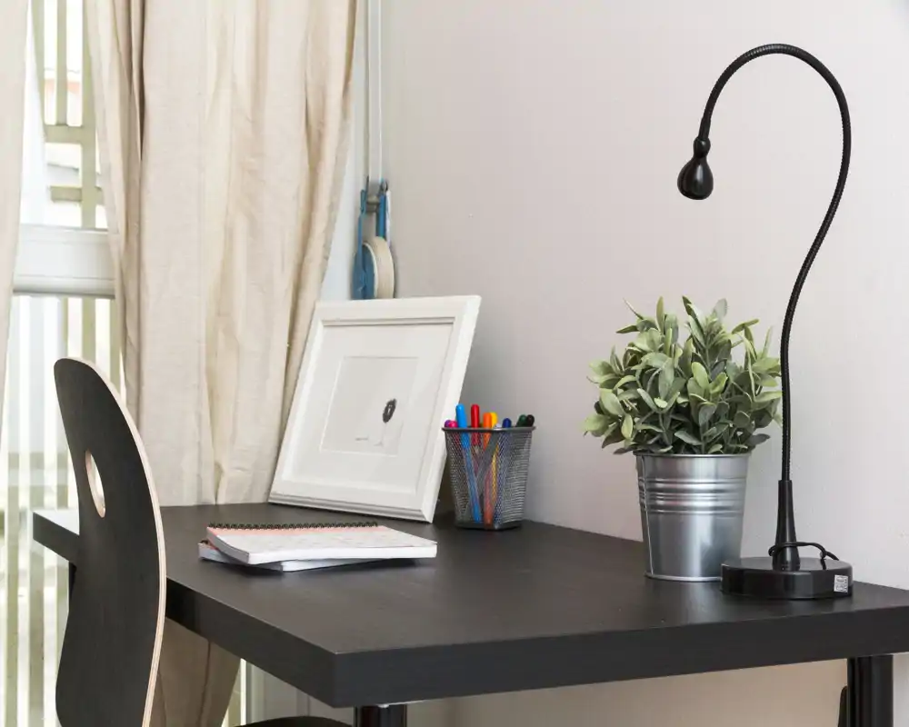 Espace de travail lumineux et soigné avec bureau en bois foncé, lampe flexible, plante en pot et fournitures — idéal pour étudier ou travailler.