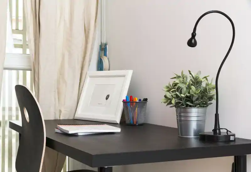 Espace de travail lumineux et soigné avec bureau en bois foncé, lampe flexible, plante en pot et fournitures — idéal pour étudier ou travailler.