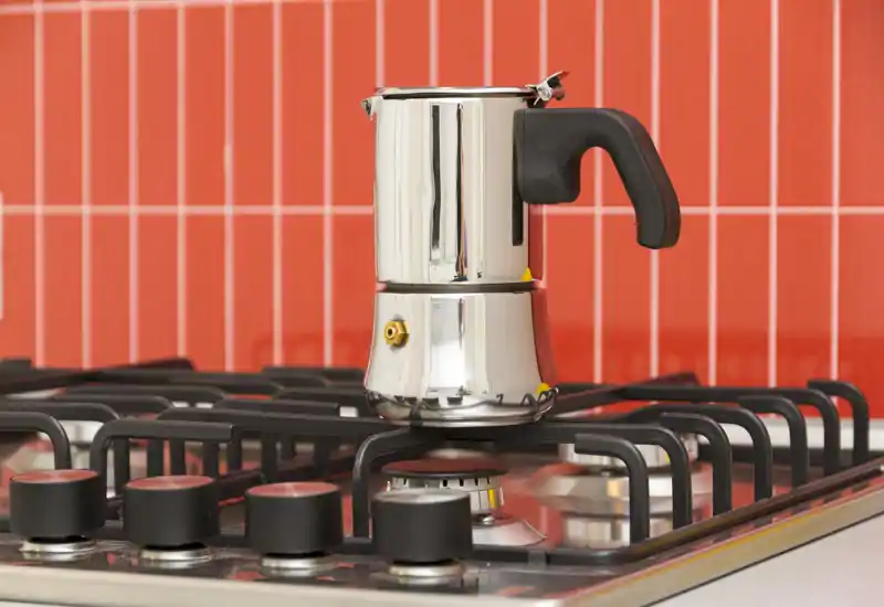 Primo piano del piano cottura con una caffettiera moka in acciaio davanti a un vivace rivestimento piastrellato rosso — dettaglio luminoso e moderno ideale per annunci incentrati sugli elettrodomestici o sulla cucina.