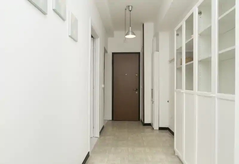 Ingresso luminoso e minimal con porta centrale in legno e armadi bianchi a muro sulla destra — corridoio semplice e ben illuminato ideale per un annuncio.