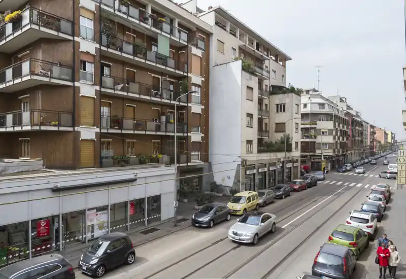 Vista esterna su strada che mostra un isolato urbano con auto parcheggiate, binari del tram e balconi residenziali — ideale per evidenziare la posizione e l’accesso dalla strada.