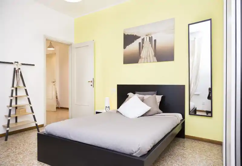 Bright, modern bedroom with a double bed, decorative pillows, a bedside lamp and wall art; clean, well-styled and suitable for rental listing photos.