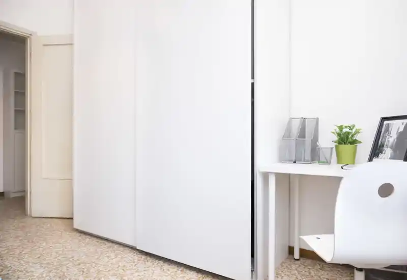 Minimal, bright room corner with a large white wardrobe and a small desk area with a plant — clean, modern storage and workspace.