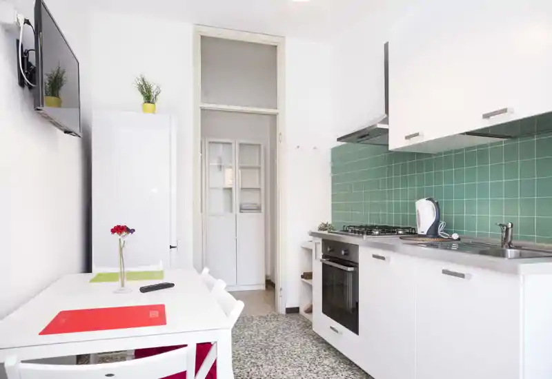 Modern compact kitchen with white cabinets, green tile backsplash, built-in oven and a small dining table — bright, tidy and well-equipped for short stays.