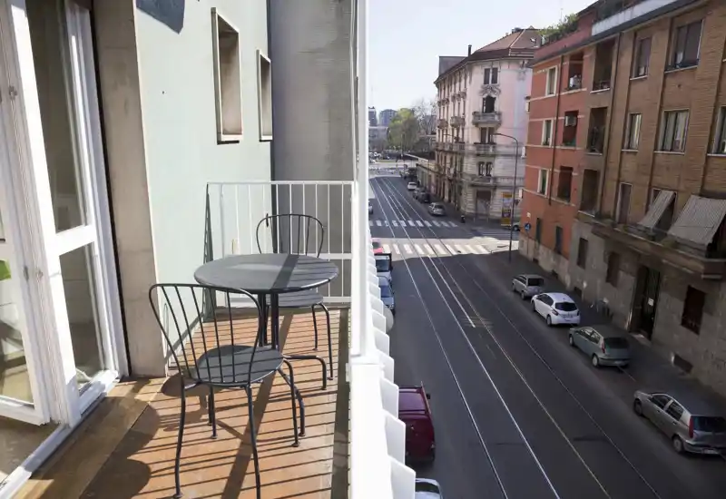 Sunny narrow balcony with a small round table and two metal chairs, overlooking a city street — ideal for morning coffee.