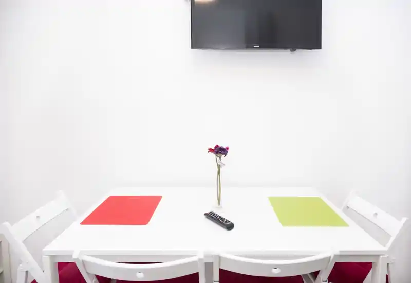 Bright, minimalist dining area with a white table, four chairs, colorful placemats and a small vase — ideal for compact apartment listings.