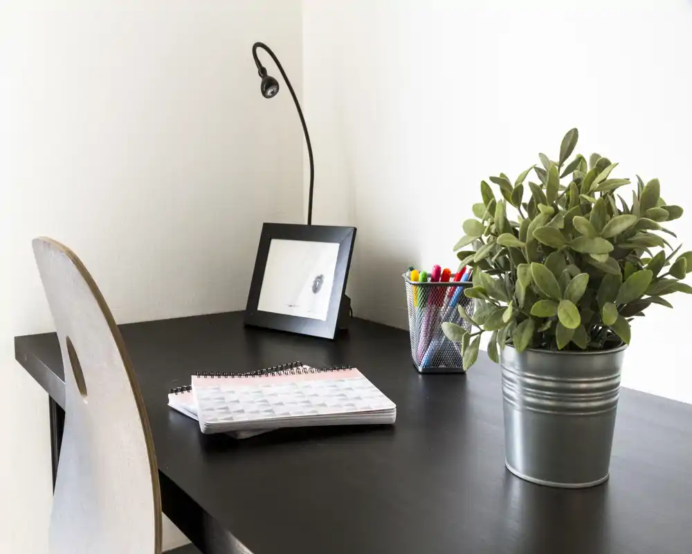 Angolo scrivania luminoso e ordinato con pianta in vaso, taccuino e lampada: ideale come spazio per smart working o studio.