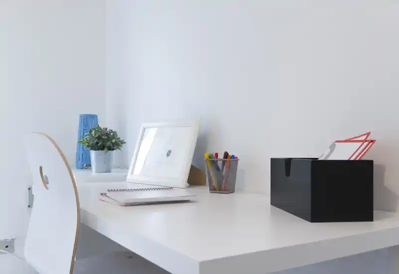 Bright, minimal home workspace with a white desk, chair, small plant, framed print and stationery — ideal for focused work or study.