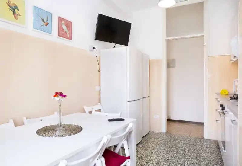Bright, well-styled kitchen with a white dining table, chairs and a tall refrigerator. Decorative wall art and a vase of flowers add a cozy touch.