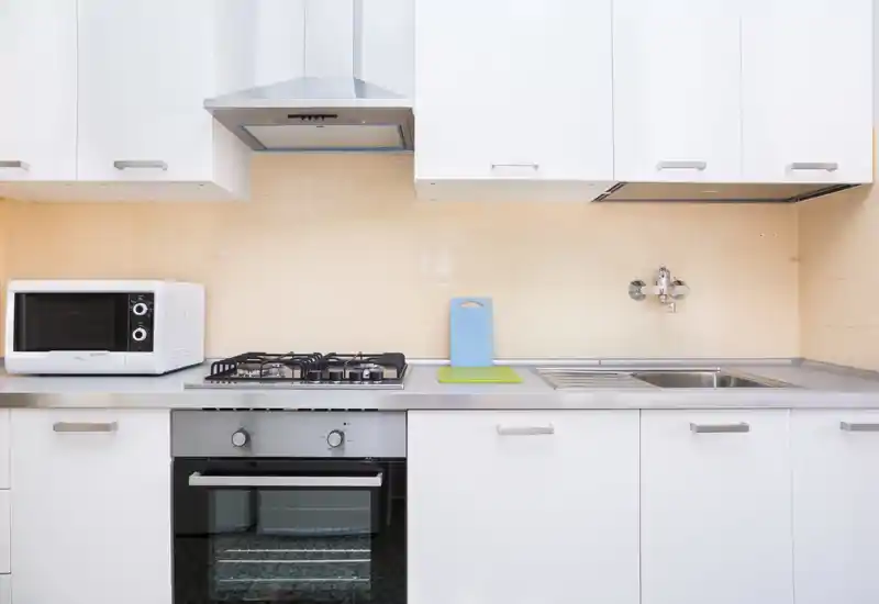 Bright, modern kitchen with stainless steel countertop, built-in oven and gas hob, microwave and sink in a clean, minimal layout.