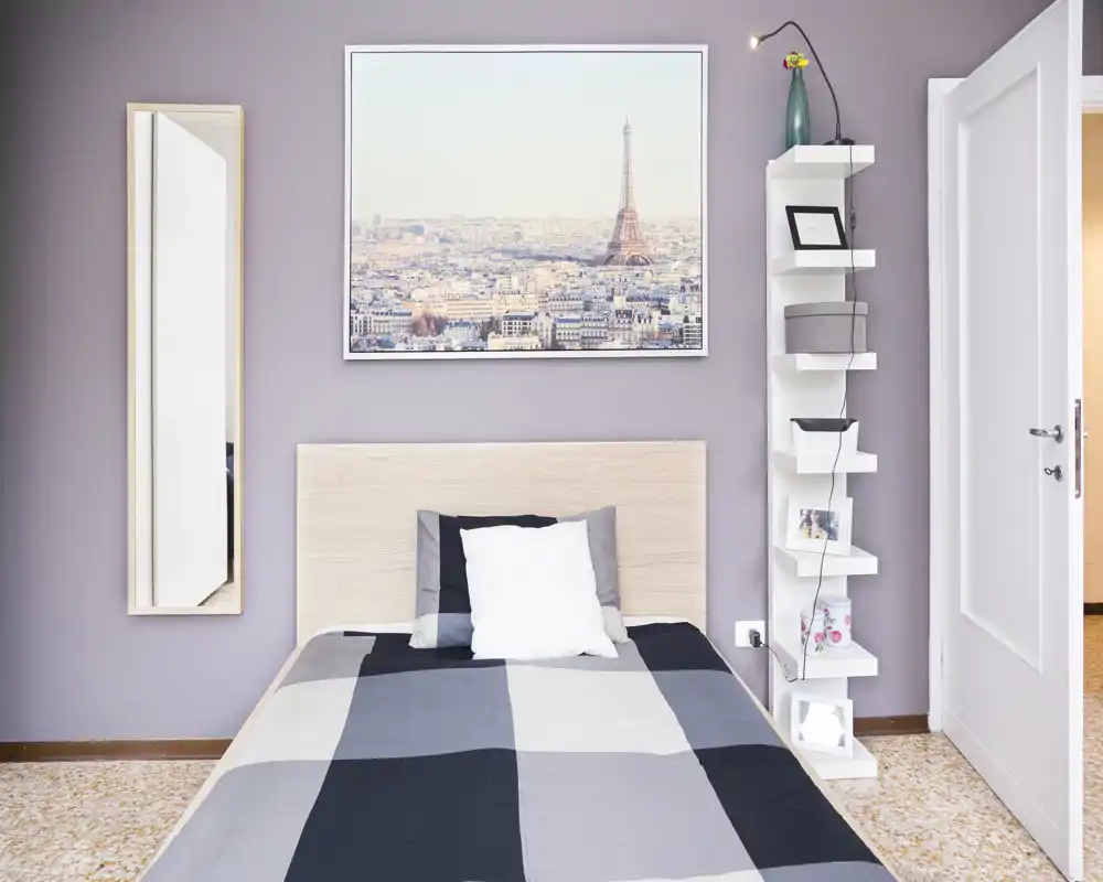 Bright, neatly styled bedroom with a full-sized bed, decorative pillows and a Paris cityscape print above the headboard. Clean lines and soft pastel walls create a calm, inviting atmosphere ideal for rental photos.