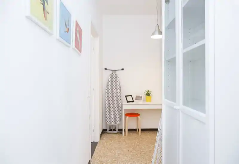 Bright, minimalist entrance hallway with a small desk, stool and ironing board — tidy space ideal for a drop zone or compact workspace.