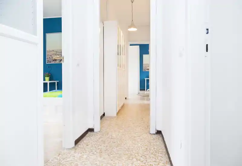 Bright, well-lit apartment corridor with white walls and terrazzo floor leading to adjacent rooms, suitable as the building entrance or hallway.