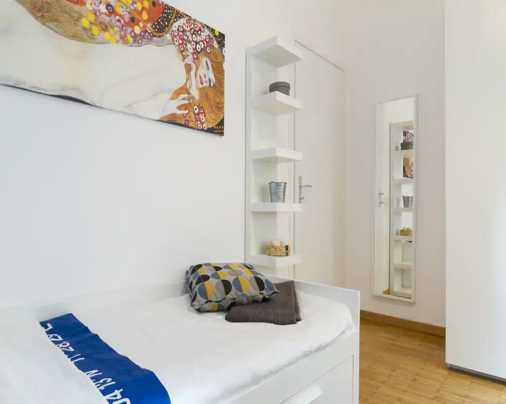 Camera singola moderna e luminosa con letto ben rifatto, cuscini decorativi e grande quadro a parete; stile minimale e pulito, ideale per un annuncio di affitto.