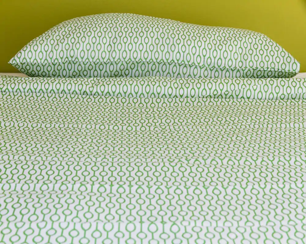 Primo piano di un letto con lenzuola bianche e verdi a motivo e un cuscino coordinato su una parete gialla; biancheria luminosa e pulita, perfetta per gli annunci.
