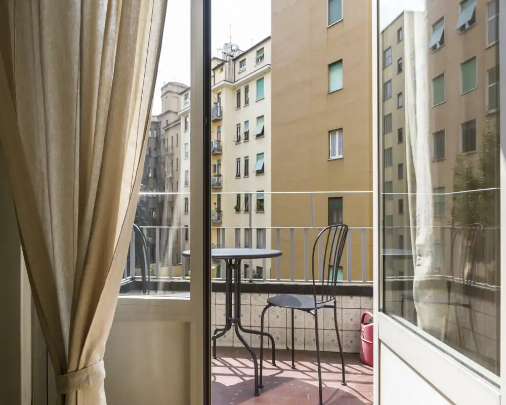 Piccolo balcone soleggiato con tavolino bistro in metallo e due sedie, affacciato sulla città — perfetto per il caffè mattutino.