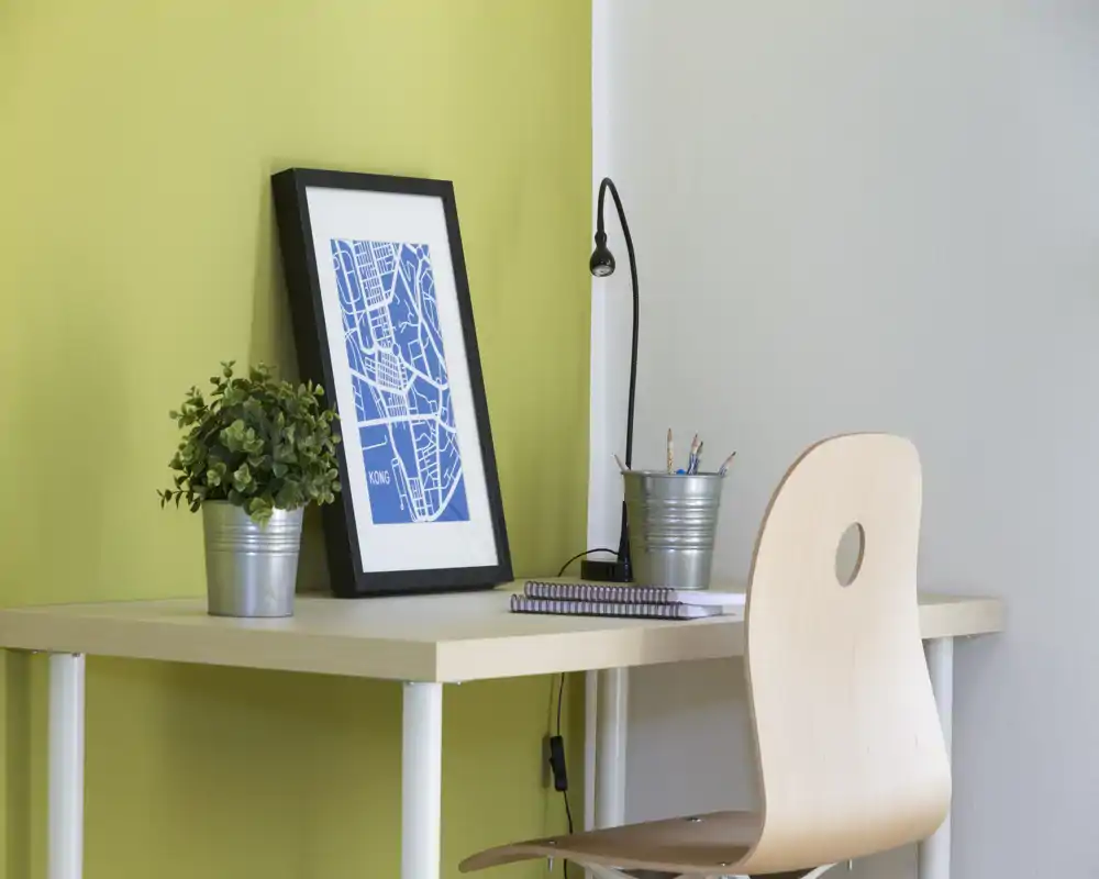 Area di lavoro compatta e curata con scrivania in legno chiaro, sedia, lampada da tavolo e dettagli decorativi — perfetta per studiare o lavorare da casa.