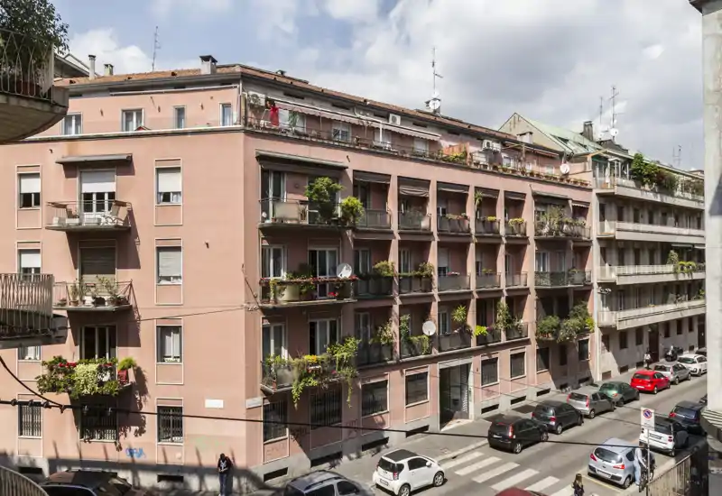 Vista su strada di un edificio residenziale con balconi, piante e auto parcheggiate in pieno giorno — perfetta per mostrare la facciata e il quartiere.