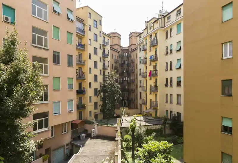 Vista di un cortile interno soleggiato tra palazzi residenziali con piccole aree a verde e balconi; tipico spazio esterno condominiale urbano.