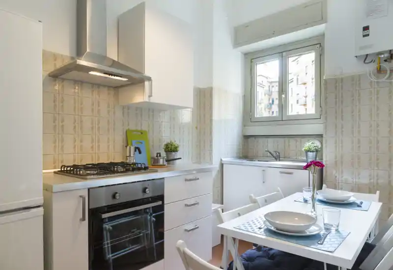 Cucina compatta e luminosa con piano cottura a gas, forno integrato e un piccolo tavolo da pranzo per due — perfetta per un appartamento in città. La luce naturale dalla finestra rende l'ambiente arioso e accogliente.