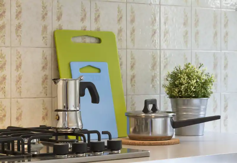 Piano di lavoro cucina luminoso e curato con piano cottura, moka, pentola, taglieri e piccolo vaso decorativo — pulito e accogliente per cucinare.