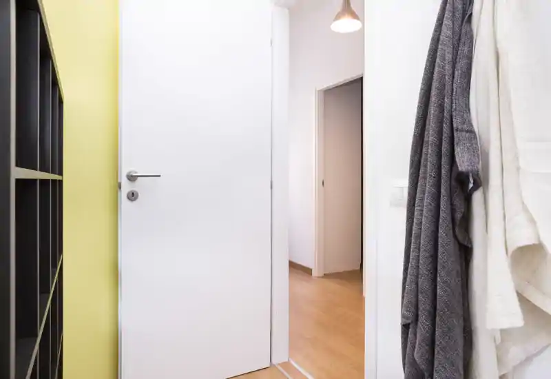 Ingresso luminoso e ordinato con porta bianca, attaccapanni e mobile a scaffali—ben illuminato e accogliente.
