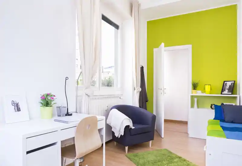 Camera da letto moderna e luminosa con letto confortevole, poltrona accogliente, scrivania e arredi colorati: perfetta per un annuncio che valorizzi la luce naturale e la disposizione funzionale.